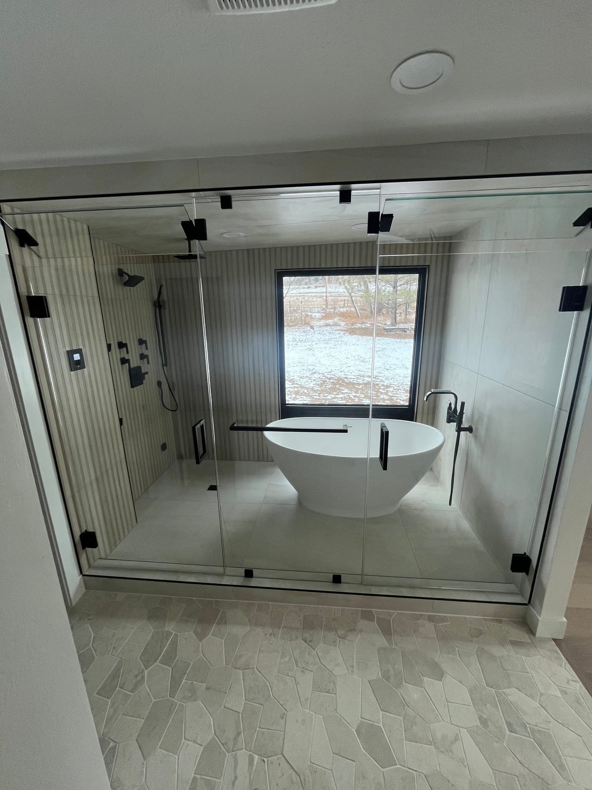 Glass-enclosed wet room with a freestanding tub and matte-black shower fixtures