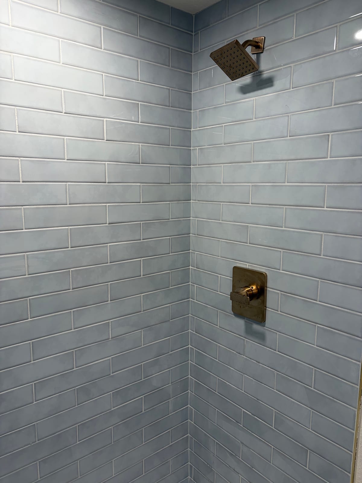 Brass showerhead and matching valve trim against gray subway tile