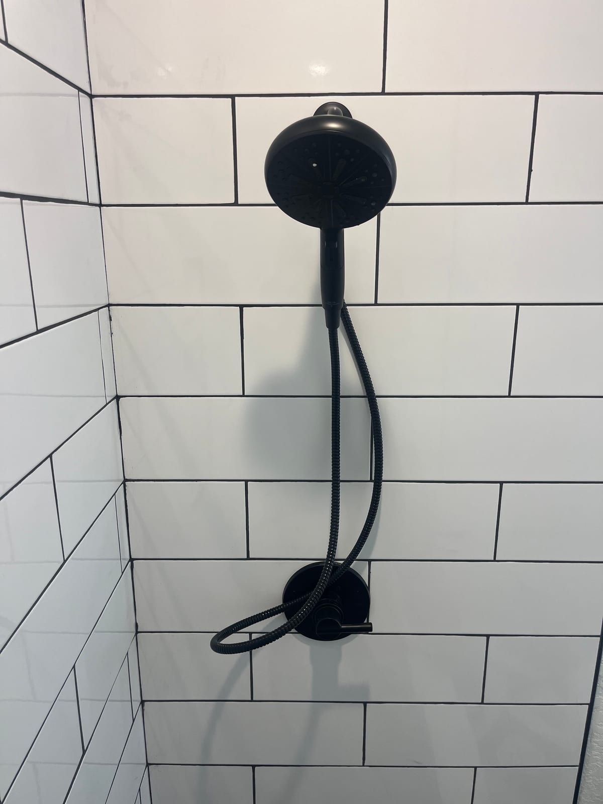 Matte-black handheld shower and valve trim against white tile