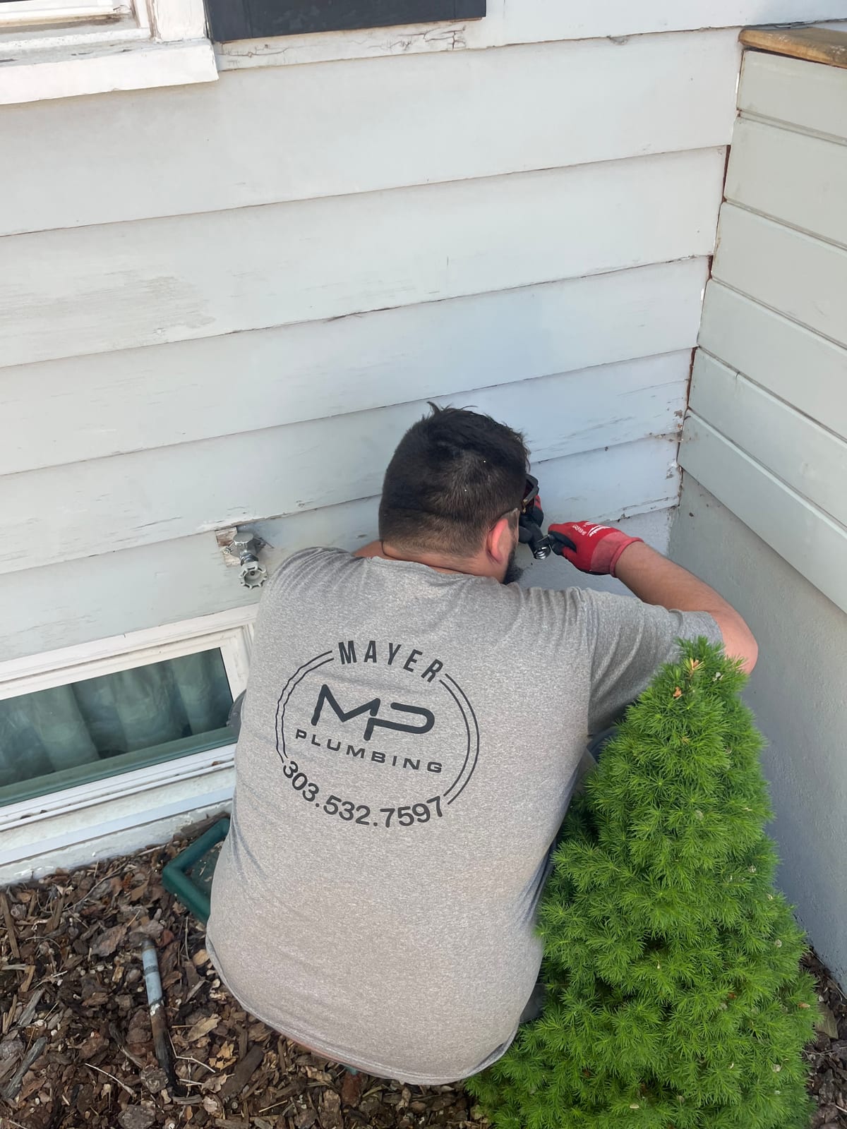 Mayer Plumbing technician working at an outdoor faucet on white siding