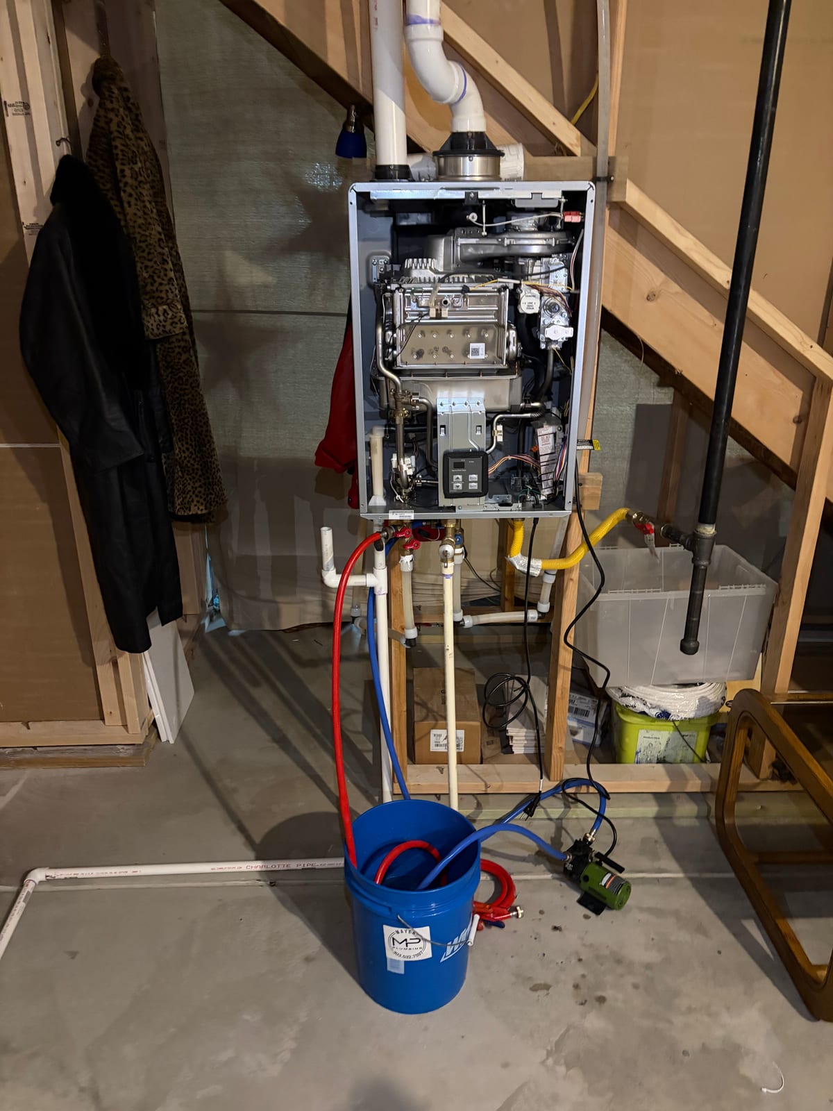 Tankless water heater with its cover removed and flushing hoses connected to a pump and bucket